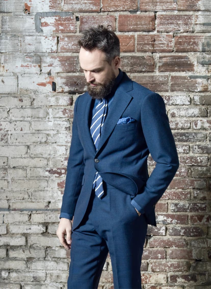 Homme en costume bleu indigo avec cravate rayée contre un mur de briques